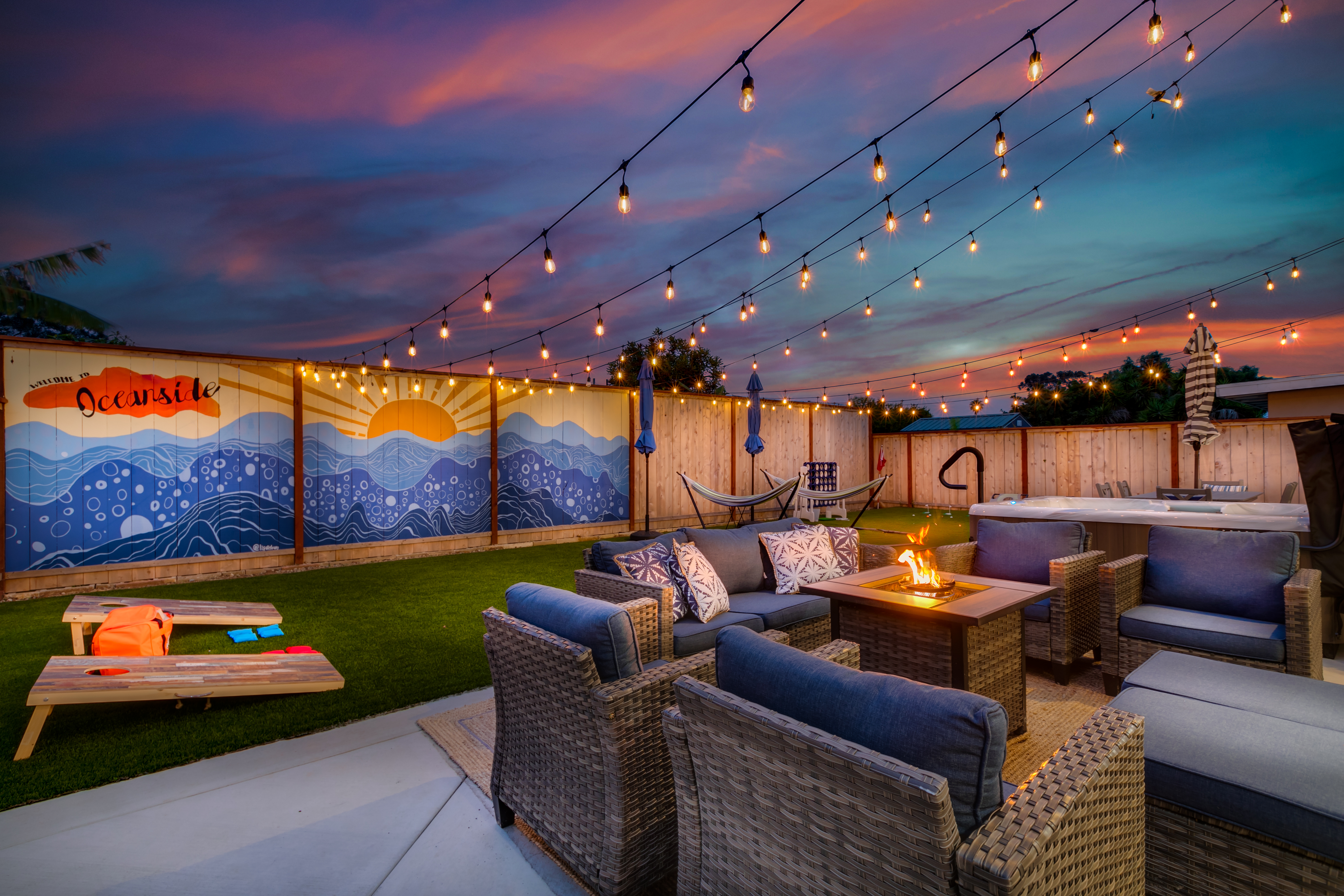 Twilight backyard with string lights, fire pit, hammocks, and Oceanside mural